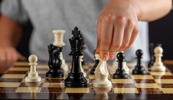 A caucasian boy is holding a white knight chess piece during a game. He will make a move. Dark background image for determination, concentration, focusing, calculation risk taking behavior concepts