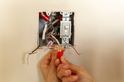 An electrician is replacing a wall switch. A DIY project concept. High voltage danger. She is working with bare hand tightening wires using plastic wirenut. There are labels on each wire 