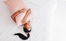 Beautiful Indonesian girl lying on a pink pillow with a silk pillowcase. View from above