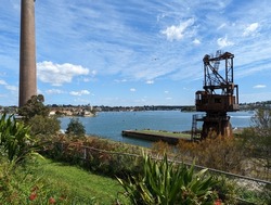 A rusty vintage crane and a very tall brick chimney that was attached to the coal power station built to supply the dockyards at the naval base on Cockatoo island, Sydney, Australia.