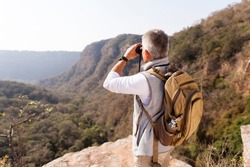 middle aged male hiker using binoculars on top of the mountain