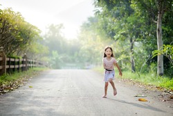 Portrait little cute Asian girl running under the tree on the old road in the morning with sunshine