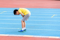 Young Asian boy tired on blue track after running in the stadium during day time to practice himself.
