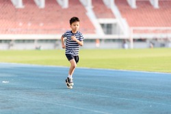 Young Asian boy running on blue track in the stadium during day time to practice himself.