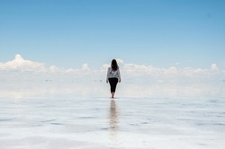 woman walking in the salt flats on the mirrored water, celestial sky, heat, mountains and clouds