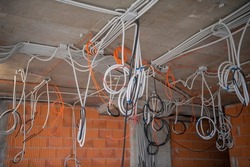 interior of skyscraper floor under construction. Cables, pipes and tubes hanging from ceiling of room. Building under construction, work in progress. Placement of electrical wires and cables.