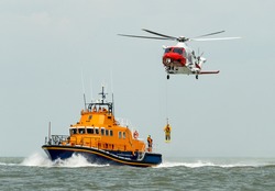 orange sea rescue boat at sea off south coast of Britain man being winched to emergency rescue helicopter