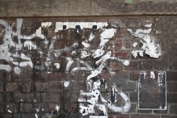 Urban old shabby weathered brick wall with graffiti tag scribbles and torn street posters