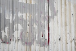 Industrial ghetto style abandoned corrugated metal fence texture with painted over graffiti 