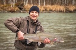A happy fisherman holding up a fresh steelhead, rainbow trout, with a predator scar on its side, from the Kalum River, near Terrace, British Columbia, Canada
