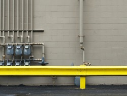 wall pipes in back alley with yellow guard rail and black concrete