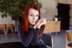 portrait of a red-haired young girl with blue eyes. Attractive redhead girl with pale skin and natural make-up posing for the camera in a cafe