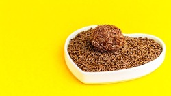 Brigadeiro over a heart-shaped bowl on a yellow background. I love brigadier.