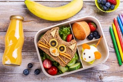 Kids lunch box with cute cat sandwich, muffin and mouse made from boiled egg. Back to school breakfast background - lunch box, bottle of orange juice and green apple. Top view. Copy space