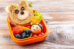 Kids lunch box with funny bear sandwich and boiled egg bee, apple, orange juice. Back to school background. Copy space