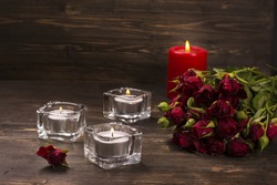 Romantic greeting card: bunch of roses and candles over dark wooden background. Selective focus