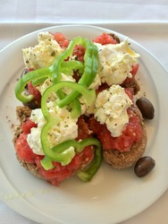 Dakos traditional Greek appetizer on a white plate with olive oil, dry rye bread, olives, feta cheese and tomatoes. Healthy eating concept. Mediterranean lifestyle.