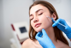 Beautician doctor with botulinum toxin syringe making injection to to remove crow's feet. Cheek volume enhance mesotherapy. Anti-aging treatment and face lift in cosmetology clinic.
