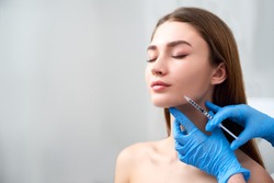 Smile lifting and lip augmentation. Beautician doctor hands doing beauty procedure to female face with syringe. Young woman's mouth countouring with filler injection. Marionette lines treatment.