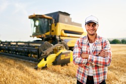 Portrait of proud harvester machine driver with hands crossed on chest. Farmer standing at his combine. Agronomist looking at camera. Rancher at harvesting work on stubble of harvested wheat field.