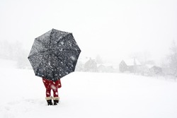 A woman stand alone in snow storm watching  falling snow in the village, Red dress woman holding black umbrella standing in snow storm, Lonely woman in the winter wonderland