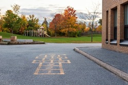 School building and schoolyard with playground for children in evening in fall season. Selective focus on hopscotch. Back to school educational concept