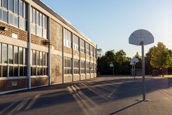 Schoolyard with basketball court and school building exterior in the sunny evening. School yard with playground