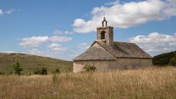 Small stone chapel in the mountains of southern France. Religious building on the top of a grassy hill. Summer light, blue sky with white clouds. Calm, peace, religious piety and concern