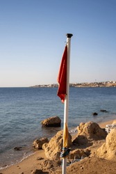red warning flag and pole with the blue sea in the background 