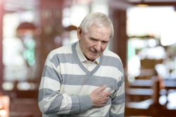 Old man holding breast because of heart infarction. Painful senior man with pain on heart, heart attack. Abstract blurred background.