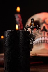 Burning candle with black metallic cross with humans skull. Satanic wicca death ritual concept.