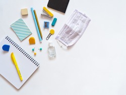 Top view of stationery supplies during covid isolated on white background. Student's desk with school supplies as notebooks and face mask. Back to school concept during coronavirus. Copy space.