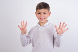 Cute Caucasian kid boy wearing knitted sweater against white wall showing and pointing up with fingers number nine while smiling confident and happy.