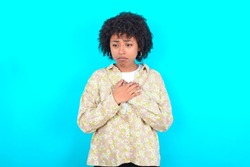 Sad young girl with afro hairstyle wearing floral shirt over blue background desperate and depressed with tears on her eyes suffering pain and depression  in sadness facial expression and emotion 