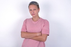 Serious pensive Caucasian woman with short hair wearing pink T-shirt over white wall feel like cool confident entrepreneur cross hands.