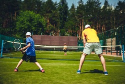 Full length little boy and man playing tennis with competitor. They turning back to camera while locating opposite net outside