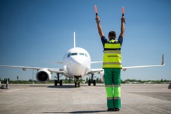 Flight is over. Back view of airport worker meeting passengers and directing the plane. Blue sky, aircraft and runway on background