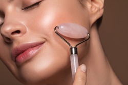 Close up photo of a young woman looking relaxed and smiling while using a natural rose quartz face roller
