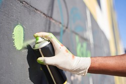 Close up of the hand of multiracial man wearing dirty disposable gloves holding spray paint can while drawing live murales. Urban lifestyle and artist concept