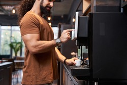 Close up view of the startup coworker man making coffee during office break time while standing near the coffee machine and pushing at the button with his finger