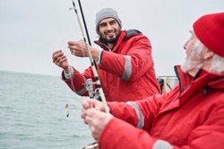 Professional fishing. Waist up portrait view of the unshaven young man telling something to his senior colleague while preparing to the fishing. Stock photo