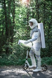 Confident spaceman wearing white armor is standing near scooter and holding map. He looking forward. Profile
