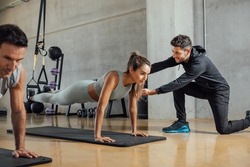 Personal trainer corrects woman's plank position at gym.