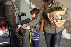 Mother and son charging electric car at home. 