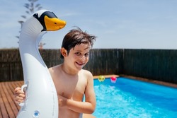 Happy cute child stands next to a swimmingpool and holds swan inflatable ring