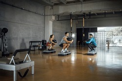 Male Instructor giving fitness class to sporty man and woman working out in dark big gym with fitness ball. Sport, training and lifestyle concept Horizontal copy-space, wide angle, full length