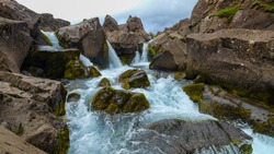 Beautiful landscape with a waterfall on a small mountain river in Iceland.  Clear Water flows in a stormy stream among stones and rocks covered with moss