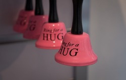 Decorative bells with a funny and amusing message that says ring for a hug. Pink bells in a gift shop. Bells hung in a row.