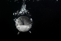Alarm clock in water. Concept of time. Clock falls into the water with a splash and air bubbles. Plenty of space for text.