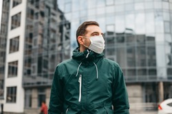 portrait of brunette man in a surgical bandage on a background of a modern building, coronavirus, illness, infection, quarantine, medical mask